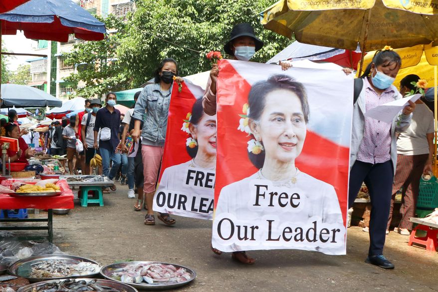 Protesters walk through a market with posters of ousted Myanmar leader Aung San Suu Kyi at Kamayut township in Yangon, Myanmar, on April 8, 2021. A Myanmar court convicted Suu Kyi in more corruption cases Monday, Aug. 15, 2022, adding six years to prison sentence. (AP Photo, File)
