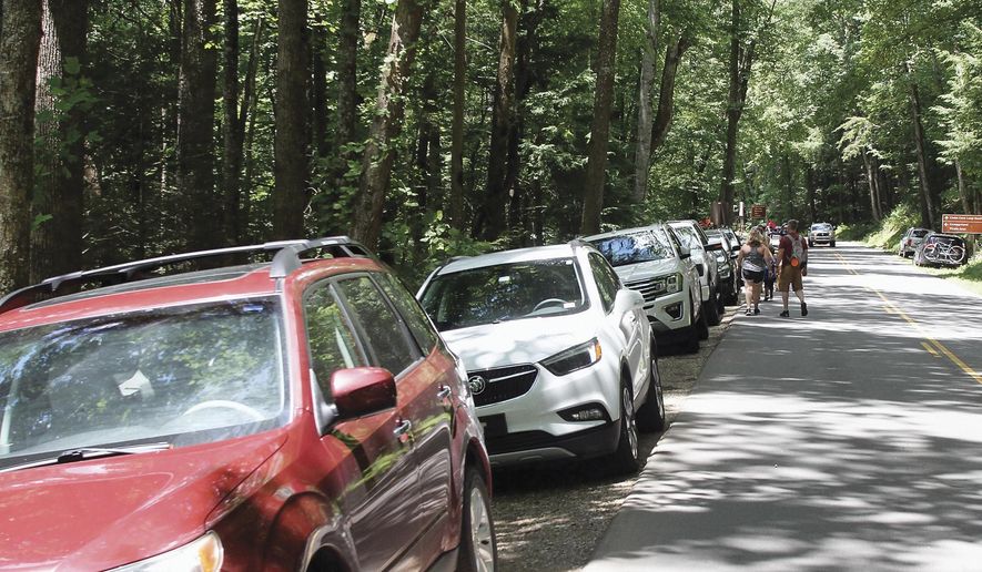 Visitors walk down Laurel Creek Road to Cades Cove after parking along the road because parking lots around the Cove were full, on June 24, 2020, in The Great Smoky Mountains National Park. Beginning March 2023, visitors to Great Smoky Mountains National Park will need to purchase a parking pass to use the facilities. (Tom Sherlin/The Daily Times via AP, File)