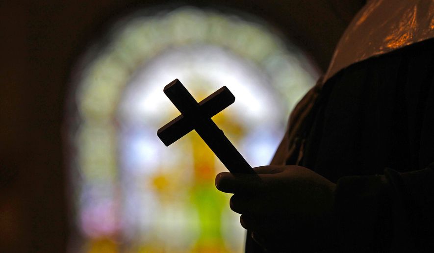 This Dec. 1, 2012 file photo shows a silhouette of a crucifix and a stained glass window inside a Catholic Church in New Orleans. (AP Photo/Gerald Herbert, File)