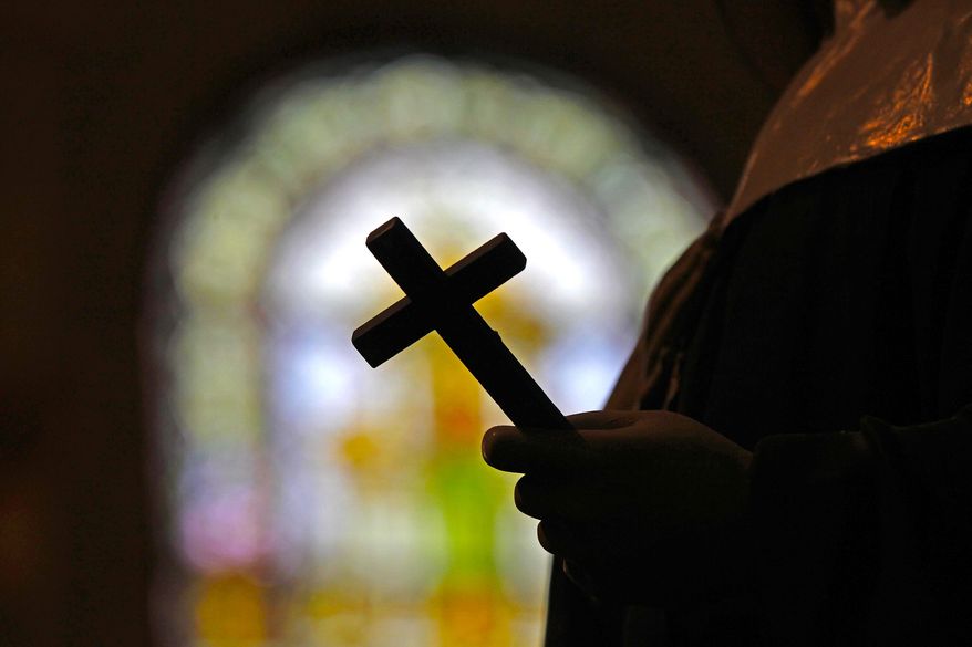 This Dec. 1, 2012 file photo shows a silhouette of a crucifix and a stained glass window inside a Catholic Church in New Orleans. (AP Photo/Gerald Herbert, File)