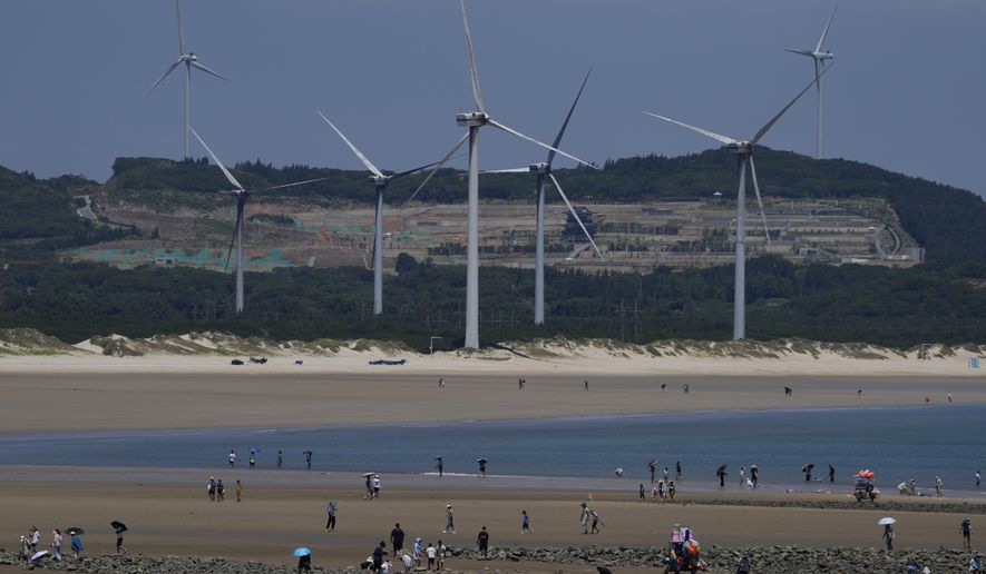 Beachgoers walk near wind turbines along the coast of Pingtan in Southern China&#39;s Fujian province, on Aug. 6, 2022. The world&#39;s two biggest emitters of greenhouse gases are sparring on Twitter over climate policy, with China asking if the U.S. can deliver on the landmark climate legislation signed into law by President Joe Biden this week. (AP Photo/Ng Han Guan)