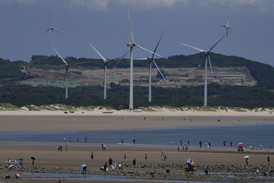 Beachgoers walk near wind turbines along the coast of Pingtan in Southern China's Fujian province, on Aug. 6, 2022. The world's two biggest emitters of greenhouse gases are sparring on Twitter over climate policy, with China asking if the U.S. can deliver on the landmark climate legislation signed into law by President Joe Biden this week. (AP Photo/Ng Han Guan)