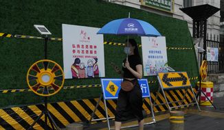 A woman wearing mask walks past construction warning sign during a rainy day in Beijing, Thursday, Aug. 18, 2022. Some were killed with others missing after a flash flood in western China Thursday, as China faces both summer rains and severe heat and drought in different parts of the country. (AP Photo/Ng Han Guan)