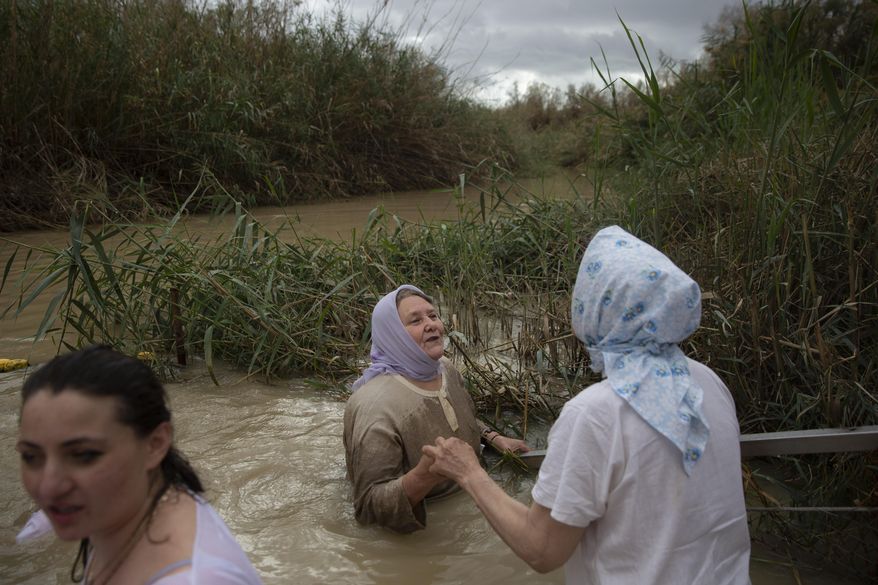 FILE - Christian pilgrims stand in the waters of the Jordan River during a baptism ceremony as part of the Orthodox Feast of the Epiphany at the Qasr al-Yahud baptismal site, near the West Bank town of Jericho, on Friday, Jan. 19, 2018. Tourists and pilgrims come to the river from near and far, many driven by faith, to follow in Christ’s footsteps, to touch its water, to conjure up biblical events. (AP Photo/Oded Balilty)