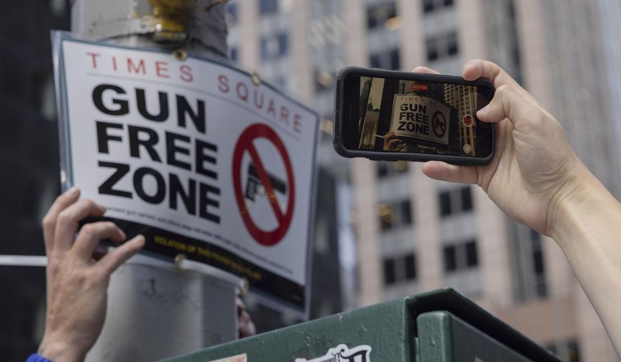 A person takes picture of an New York Police Department Public Affairs officer setting up signs reading Gun Free Zone around Times Square, Wednesday, Aug. 31, 2022, in New York. (AP Photo/Yuki Iwamura)
