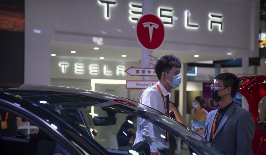 Staff members talk near vehicles at a display for automaker Tesla at the China International Fair for Trade in Services (CIFTIS) in Beijing, Friday, Sept. 2, 2022. (AP Photo/Mark Schiefelbein)