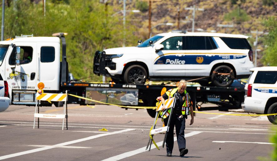 A police officer carries traffic barricades across 27th Avenue near Dear Valley Road, Sunday, Aug. 29, 2022, in Phoenix, as a damaged police vehicle is transported out of the area after a shooting occurred the night before injuring two Phoenix police officers. Americans struggled this week to process not one, but multiple high-profile shootings that unfolded in major cities and smaller towns across the U.S. But behind the stand-out headlines about shooting rampages in Bend, Ore., Phoenix, Detroit and Houston were dozens of murders and violent crimes that went largely unnoticed. (Megan Mendoza/The Arizona Republic via AP)