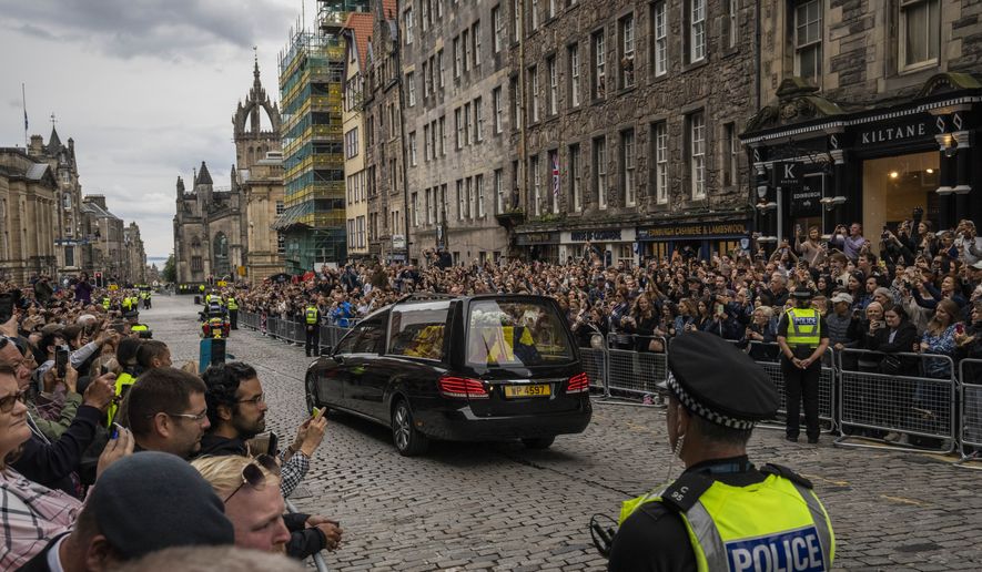 People watch the Queens cortege with the hearse containing her coffin on the Royal Mile in Edinburgh, Scotland, Sunday, Sept. 11, 2022. The coffin of the late Queen Elizabeth II is being transported Sunday on a journey from Balmoral to the Palace of Holyroodhouse in Edinburgh, where it will lie at rest before being moved to London later in the week. (AP Photo/Bernat Armangue)