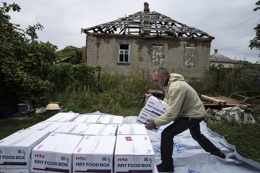 A man sorts humanitarian aid in front of a house destroyed by Russian attack in the recently retaken area of Izium, Ukraine, Wednesday, Sept. 14, 2022. (AP Photo/Evgeniy Maloletka)