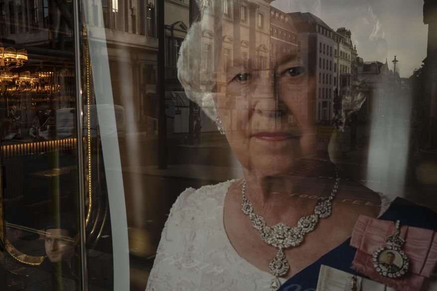 A man sits inside a restaurant displaying a portrait of the late Queen Elizabeth II in London, Sunday, Sept. 18, 2022. The Queen will lie in state in Westminster Hall for four full days before her funeral on Monday Sept. 19. (AP Photo/Felipe Dana)