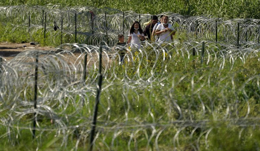 Migrants walk along concertina wire toward Border Patrol officers after illegally crossing the Rio Grande from Mexico into the U.S. at Eagle Pass, Texas, Friday, Aug. 26, 2022. The number of Venezuelans, Cubans and Nicaraguans taken into custody at the U.S. border with Mexico soared in August as migrants from Mexico and traditional sending countries were stopped less frequently, authorities said Monday. (AP Photo/Eric Gay, File)