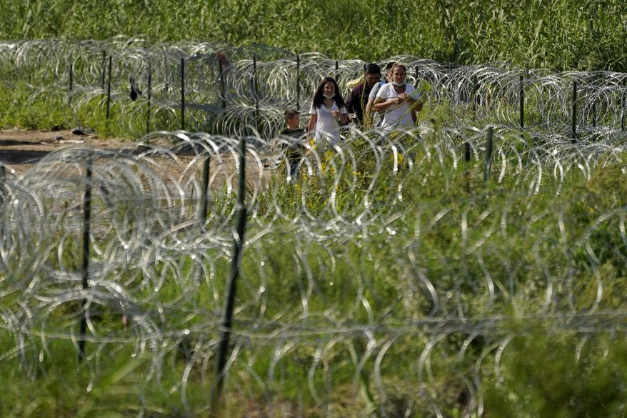 Migrants walk along concertina wire toward Border Patrol officers after illegally crossing the Rio Grande from Mexico into the U.S. at Eagle Pass, Texas, Friday, Aug. 26, 2022. The number of Venezuelans, Cubans and Nicaraguans taken into custody at the U.S. border with Mexico soared in August as migrants from Mexico and traditional sending countries were stopped less frequently, authorities said Monday. (AP Photo/Eric Gay, File)