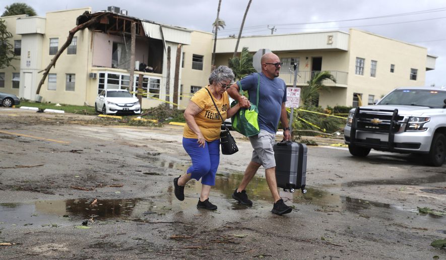 King Point resident Maria Esturilho is escorted by her son Tony Esturilho as they leave behind the damage from an apparent overnight tornado spawned from Hurricane Ian at Kings Point 55+ community in Delray Beach, Fla., on Wednesday, Sept. 28, 2022.  (Carline Jean /South Florida Sun-Sentinel via AP)