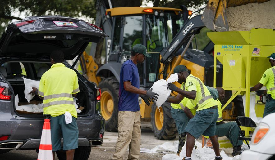 Eric Byrd hands a sandbag to Clifford Coston while working to fill people&#x27;s trucks at a sandbag station at Northwest Park, Tuesday, Sept. 27, 2022, in St. Petersburg, Fla., as Hurricane Ian approaches. (Martha Asencia-Rhine/Tampa Bay Times via AP)
