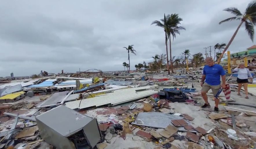 In this frame grab from video provided by Bobby Pratt, people walk along the Times Square area of Fort Meyers Beach, Fla., after Hurricane Ian tore through the area, Thursday, Sept. 29, 2022. (Bobby Pratt via AP)
