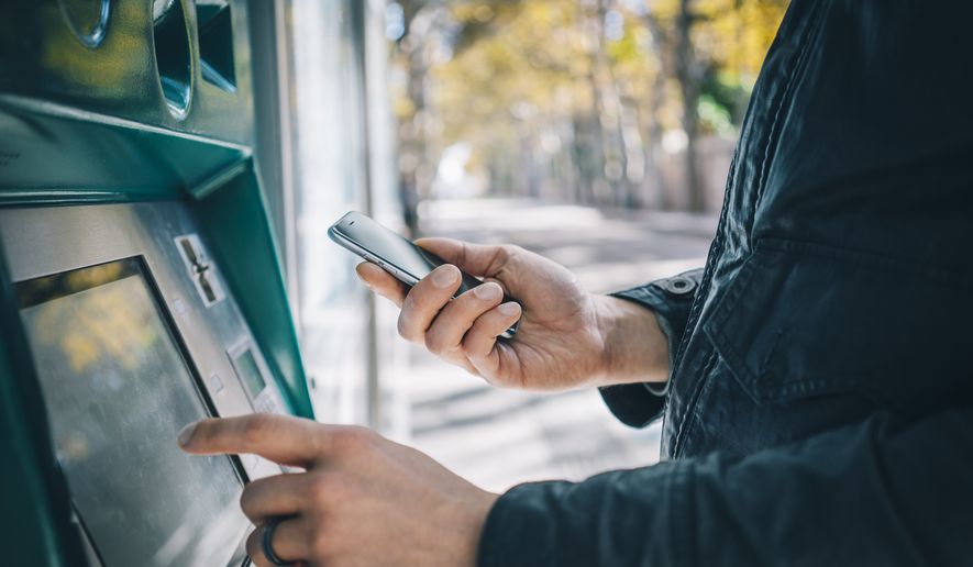 Customer using smart phone while typing on ATM, bank machine. File photo credit: Superstar via Shutterstock.