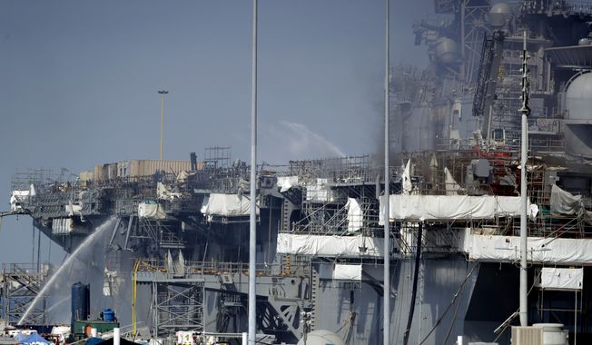 Fire crews spray water from the dock onto the side of the USS Bonhomme Richard, in San Diego, July 12, 2020. No one disputes that the Navy shares blame for the loss of the USS Bonhomme Richard, the $1.2 billion amphibious assault ship that was consumed by flames in San Diego in July 2020 as officers failed to respond quickly and its crew struggled with broken equipment. But none of that would not have happened, according to prosecution closing arguments Thursday, Sept. 29, 2022, without Ryan Sawyer Mays. (AP Photo/Gregory Bull, File)
