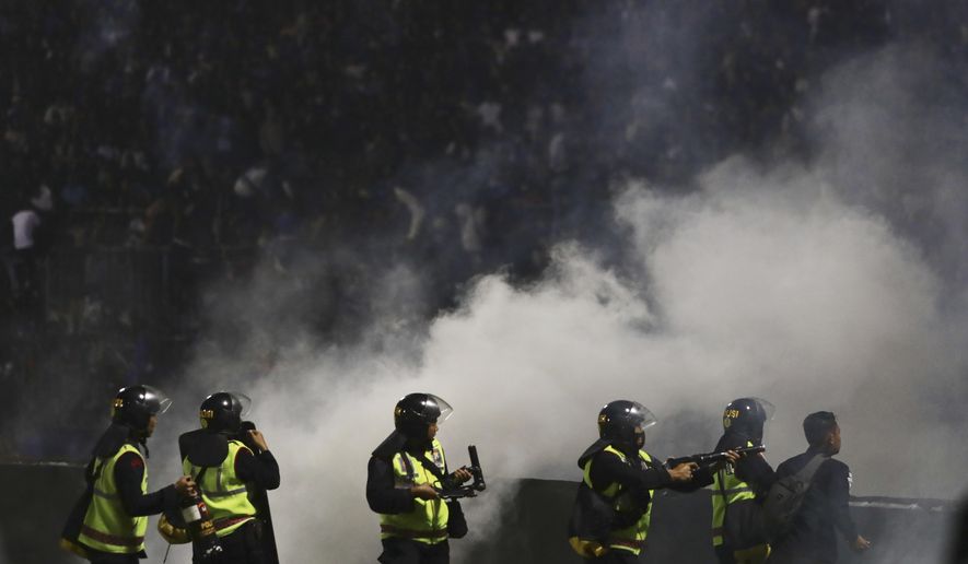 Police officers fire tear gas during a soccer match at Kanjuruhan Stadium in Malang, East Java, Indonesia, Saturday, Oct. 1, 2022. Clashes between supporters of two Indonesian soccer teams in East Java province killed over 100 fans and a number of police officers, mostly trampled to death, police said Sunday. (AP Photo/Yudha Prabowo)