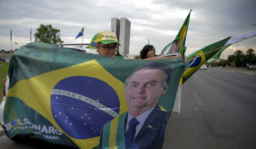 A woman holds a Brazilian flag with the image of Brazilian President Jair Bolsonaro, who is running for another term, after general election polls closed in Brasilia, Brazil, Sunday, Oct. 2, 2022. (AP Photo/Ton Molina)