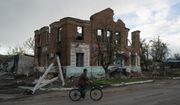 A man rides his bicycle past a damaged building in the village of Drobysheve near the recaptured town of Lyman, Ukraine, Wednesday, Oct. 5, 2022. (AP Photo/Leo Correa)