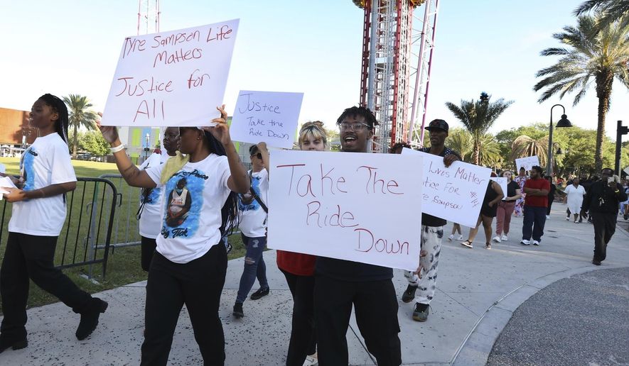 FILE - Family and supporters of Tyre Sampson march and hold signs outside the Orlando Free Fall drop tower ride at ICON Park in Orlando on March 29, 2022. A towering amusement ride in central Florida&#39;s tourism district where Tyre, 14, died when he fell to his death will be taken down because of the accident, the owner said Thursday, Oct. 6, 2022. (Stephen M. Dowell/Orlando Sentinel via AP, File)