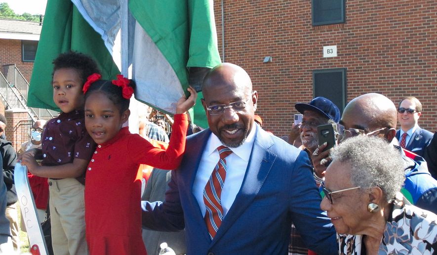 Sen. Raphael Warnock stands with his children, Caleb and Chloe, and his mother, Verlene Warnock, before unveiling a sign designating a street as Honorary Raphael Warnock Way in the senator&#39;s hometown of Savannah, Ga., Oct. 6, 2022. Warnock, a freshman Democrat, is up for reelection in November in a pivotal race against Republican and former football star Herschel Walker. (AP Photo/Russ Bynum, File)
