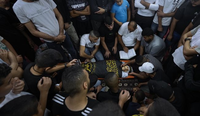 Mourners gather around the body of Palestinian Mahmoud Al-Sous, covered Islamic Jihad militant group flag, during his funeral in the West Bank town of Jenin, Saturday, Oct. 8, 2022. Israeli soldiers shot and killed two Palestinians on Saturday in an exchange of fire that erupted during a military raid in the West Bank. The Israeli military said it had arrested a 25-year-old operative from the Islamic Jihad militant group who has previously been imprisoned by Israel. It said the man had recently been involved in shooting attacks on Israeli soldiers. (AP Photo/Majdi Mohammed)