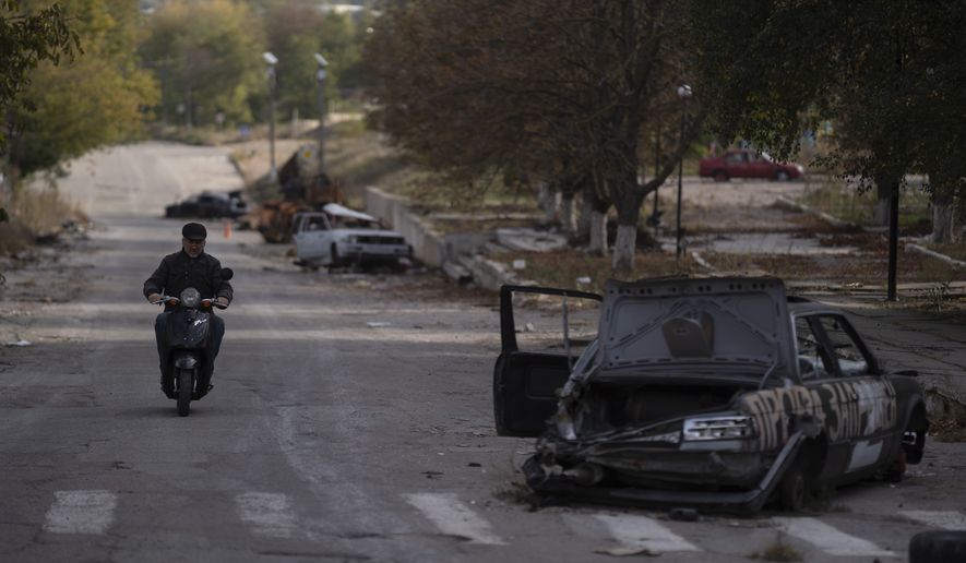 A man drives his motorcycle past destroyed cars in the retaken village of Velyka Oleksandrivka, Ukraine, Wednesday, Oct. 12, 2022. (AP Photo/Leo Correa)