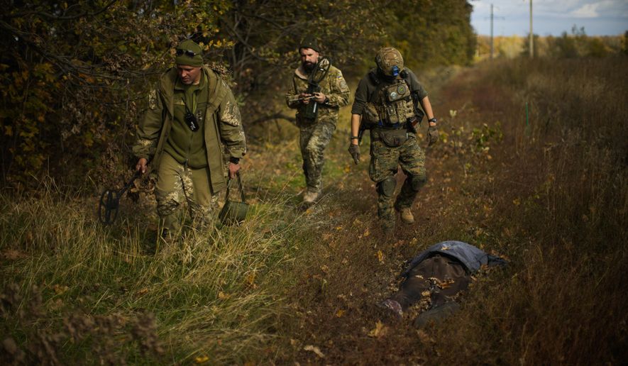 Ukrainian territorial defence deminers walk past a body of a local man who was killed after an explosion of a Russian mine near Hrakove village, Ukraine, Thursday, Oct. 13, 2022. (AP Photo/Francisco Seco)