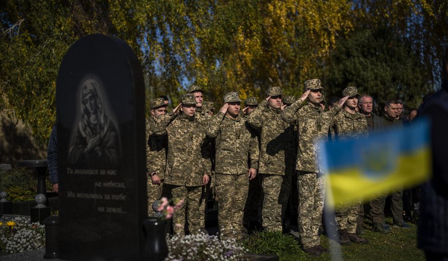 Soldiers salute as the Ukrainian national anthem is played at the funeral of Colonel Oleksiy Telizhenko in Bucha, near in Kyiv, Ukraine, Tuesday, Oct. 18, 2022. In March, Colonel Oleksiy was abducted by Russian soldiers from his home in Bucha, six months later his body was found with signals of torture buried in a forest not far away from his village. (AP Photo/Emilio Morenatti)