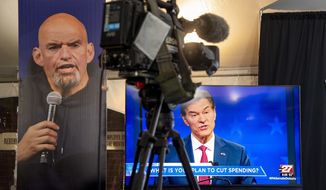 Republican Mehmet Oz, right, is seen live on a monitor in the media tent, next to a poster of Democrat John Fetterman, left, as the two U.S. Senate candidates hold their first and only debate, at the WHTM-TV/ABC 27 Studio in Harrisburg, Pa., Tuesday, Oct. 25, 2022. (Tom Gralish/The Philadelphia Inquirer via AP)