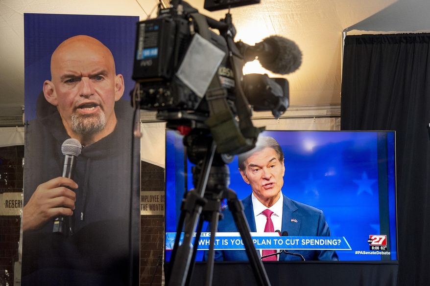 Republican Mehmet Oz, right, is seen live on a monitor in the media tent, next to a poster of Democrat John Fetterman, left, as the two U.S. Senate candidates hold their first and only debate, at the WHTM-TV/ABC 27 Studio in Harrisburg, Pa., Tuesday, Oct. 25, 2022. (Tom Gralish/The Philadelphia Inquirer via AP)