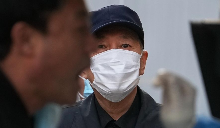 A resident wearing a face mask watches a man get his routine COVID-19 throat swab test at a coronavirus testing site in Beijing, Tuesday, Oct. 25, 2022. (AP Photo/Andy Wong)