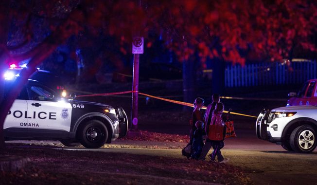 A family walks by police tape after Omaha police shot a man who drove through a barricaded area during a neighborhood Halloween celebration in Omaha, Neb., late Monday, Oct. 31, 2022. (Chris Machian/Omaha World-Herald via AP)