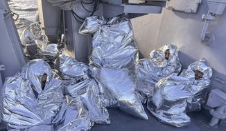 In this photo provided by the Greek Coast Guard, some of the nine men who survived a shipwreck and were found on an uninhabited islet are covered with a thermal blankets as they sit aboard a Greek Coast guard vessel, in the Aegean Sea, Greece, on Tuesday, Nov. 1, 2022. A major search and rescue operation was underway Tuesday for dozens of people missing after the boat they were on capsized and sank in stormy weather overnight off the coast of an island near the Greek capital. The coast guard said nine survivors, all men, had been found on an uninhabited islet south of the island of Evia and had been picked up by a coast guard vessel. (Greek Coast Guard via AP)