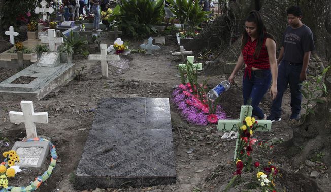 A couple walks next to one of the graves of gang members whose tombstone was destroyed on order of the government, during the Day of the Dead at the Nueva San Salvador Cemetery, in Santa Tecla, El Salvador, Wednesday, Nov. 2, 2022. Santa Tecla Mayor Henry Flores said the crews had destroyed nearly 80 tombstones in the municipal cemetery and erased gang-related graffiti. (AP Photo/Salvador Melendez)
