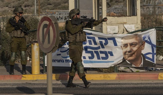 Israeli soldiers gesture to a vehicle at Tapuah Junction, next to a campaign poster for former Israeli Prime Minister Benjamin Netanyahu near the West Bank town of Nablus, Sunday, Oct. 16, 2022. (AP Photo/Tsafrir Abayov, File)