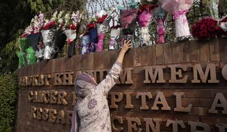 A woman places bouquet over the wall of a hospital where former Pakistani Prime Minister Imran Khan is being treated for a gunshot wound in Lahore, Pakistan, Friday, Nov. 4, 2022. Khan who narrowly escaped an assassination attempt on his life the previous day when a gunman fired multiple shots and wounded him in the leg, is listed in stable condition after undergoing surgery at a hospital, a senior leader from his party said Friday. (AP Photo/K.M. Chaudhry)