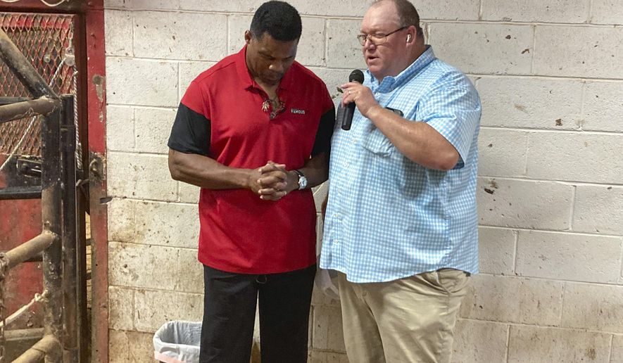 Georgia Republican Senate candidate Herschel Walker prays with a supporter at a livestock auction outside Athens, Ga., on July 20, 2022. Walker and Sen. Raphael Warnock, D-Ga., who is also a pastor at Ebenezer Baptist Church in Atlanta, both feature faith prominently in their public appeals. But the two men profess vastly different versions of Christianity. (AP Photo/Bill Barrow, File)