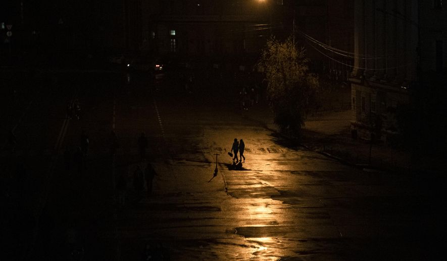 People walk across a street during a blackout in Kyiv, Ukraine, Sunday, Nov. 6, 2022. (AP Photo/Andrew Kravchenko)