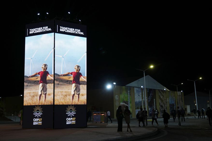 People walk past image of wind turbines at the COP27 U.N. Climate Summit, Tuesday, Nov. 8, 2022, in Sharm el-Sheikh, Egypt. (AP Photo/Peter Dejong, File)