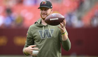 Injured Commanders quarterback Carson Wentz flips a football as he watches practice before the start of an NFL football game against the Minnesota Vikings, Sunday, Nov. 6, 2022, in Landover, Md. (AP Photo/Nick Wass)