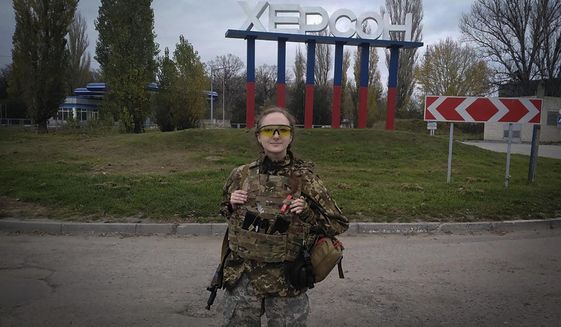 A Ukrainian female soldier poses for a photo against a Kherson sign in the background, in Kherson, Ukraine, Friday, Nov. 11, 2022. (AP Photo/Dagaz)
