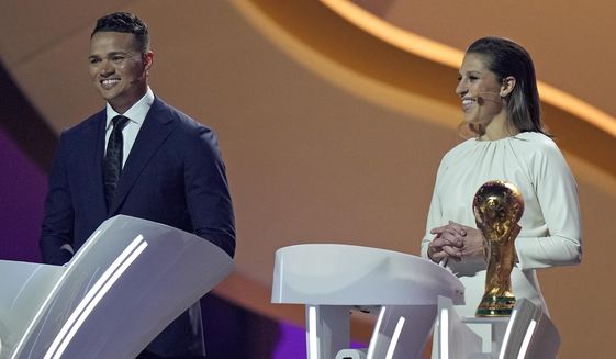 Former American soccer international Carli Lloyd, right, and Jermaine Jenas, English television presenter, pundit and retired professional soccer player assist with the 2022 soccer World Cup draw at the Doha Exhibition and Convention Center in Doha, Qatar, Friday, April 1, 2022. (AP Photo/Darko Bandic, File)