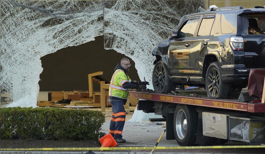 A worker secures a damaged SUV to a flatbed tow truck outside an Apple store, Monday, Nov. 21, 2022, in Hingham, Mass. At least one person was killed and multiple others were injured Monday when the SUV crashed into the store, authorities said. The crash left a large hole in the glass front of the building. (AP Photo/Steven Senne)