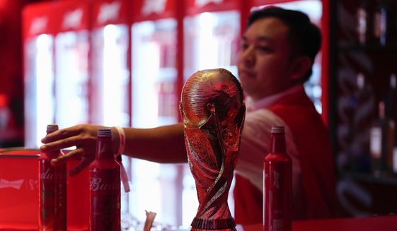 A bartender clears bottles of Budweiser beer from the bar near a replica of the FIFA World Cup trophy at an official U.S. Soccer fan party at the Budweiser World Club, in Doha, Sunday, Nov. 20, 2022. (AP Photo/Ashley Landis)