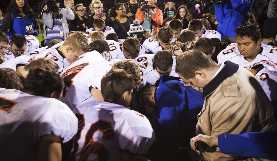 Bremerton High School assistant football coach Joe Kennedy, center in blue, kneels and prays after his team lost to Centralia in Bremerton, Wash., Oct. 16, 2015. Across America, most high school football seasons are winding down. It will wrap up the first year since the Supreme Court ruled it was OK for a public school coach near Seattle to pray on the field. (Lindsey Wasson/The Seattle Times via AP, File)
