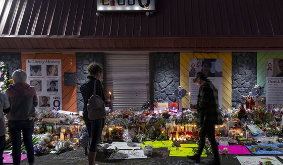 Mourners gather at a memorial outside Club Q, which has been moved from a sidewalk outside of police tape that was surrounding the club, on Friday, Nov. 25, 2022, in Colorado Spring, Colo. The memorial has been growing since Sunday morning, following a fatal shooting the night before. (Parker Seibold/The Gazette via AP)