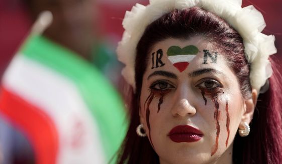 A woman stands on the tribune with her face painted in memory of Mahsa Amini, a woman who died while in police custody in Iran at the age of 22, prior to the World Cup group B soccer match between Wales and Iran, at the Ahmad Bin Ali Stadium in Al Rayyan , Qatar, Friday, Nov. 25, 2022. (AP Photo/Frank Augstein)