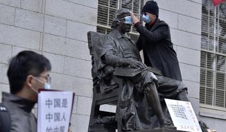 A man places a mask over the eyes of the John Harvard Statue in Harvard Yard as close to 100 students and faculty demonstrated against strict anti-virus measures in China, Tuesday, Nov. 29, 2022, at Harvard University in Cambridge, Mass. Protests in China, which were the largest and most wide spread in the nation in decades, included calls for Communist Party leader Xi Jinping to step down. (AP Photo/Josh Reynolds)
